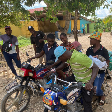 Community members gathering around motorcycles in a rural village to coordinate maternal health transport and family support services.