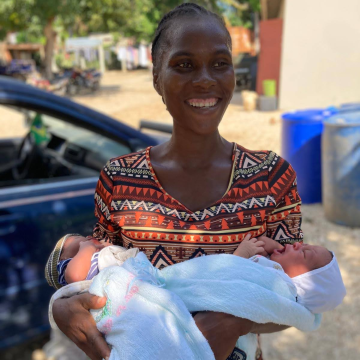 A smiling mother named Adeline holding her newborn twins, showcasing the success of Many Hands’ neonatal care and maternal health programs in Pignon.