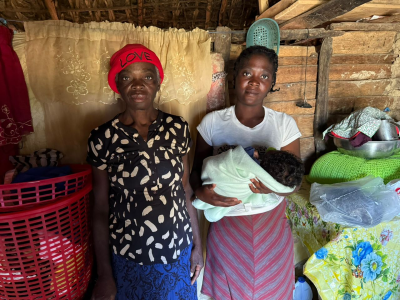 A mother and grandmother holding a newborn infant in a rural home, representing Many Hands' maternal health and family support programs in Haiti.