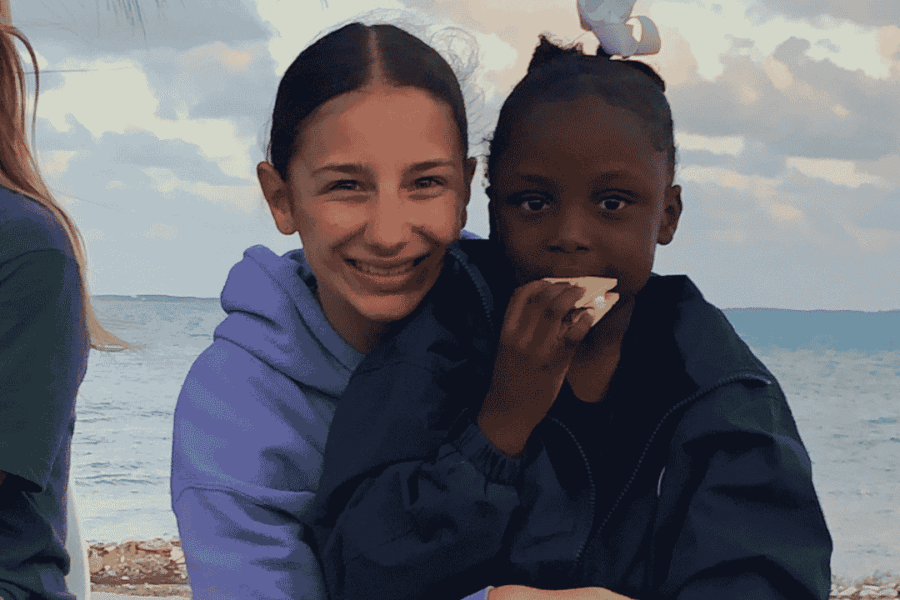 Young Impact Trip participant smiling with a local girl in Abaco by the beach