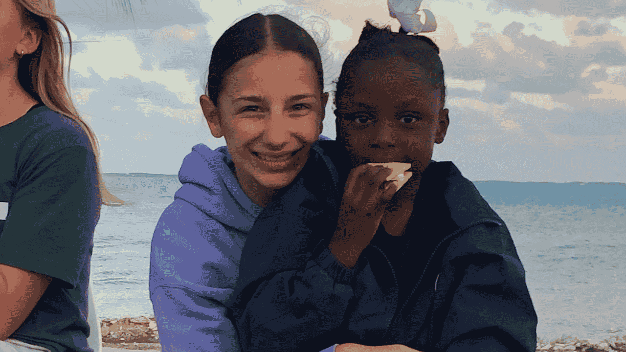 Young Impact Trip participant smiling with a local girl in Abaco by the beach