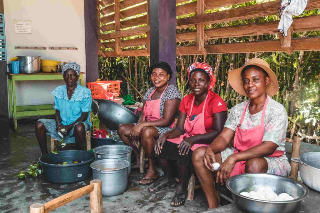 Haitian women prepare communal meals at a Many Hands campus, showcasing the collaborative local food initiatives and feeding programs that sustain families in Sylvain, Haiti.