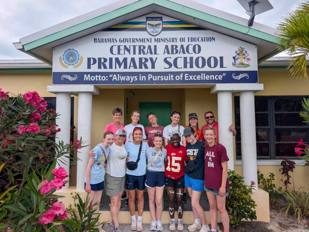 The Des Moines Christian School (DMC) impact team poses together under the entrance sign at Central Abaco Primary School (CAPS) during a youth mobilization and education trip with Many Hands.