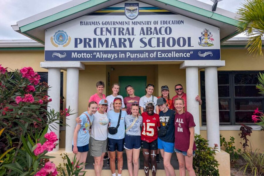 The Des Moines Christian School (DMC) impact team poses together under the entrance sign at Central Abaco Primary School (CAPS) during a youth mobilization and education trip with Many Hands.