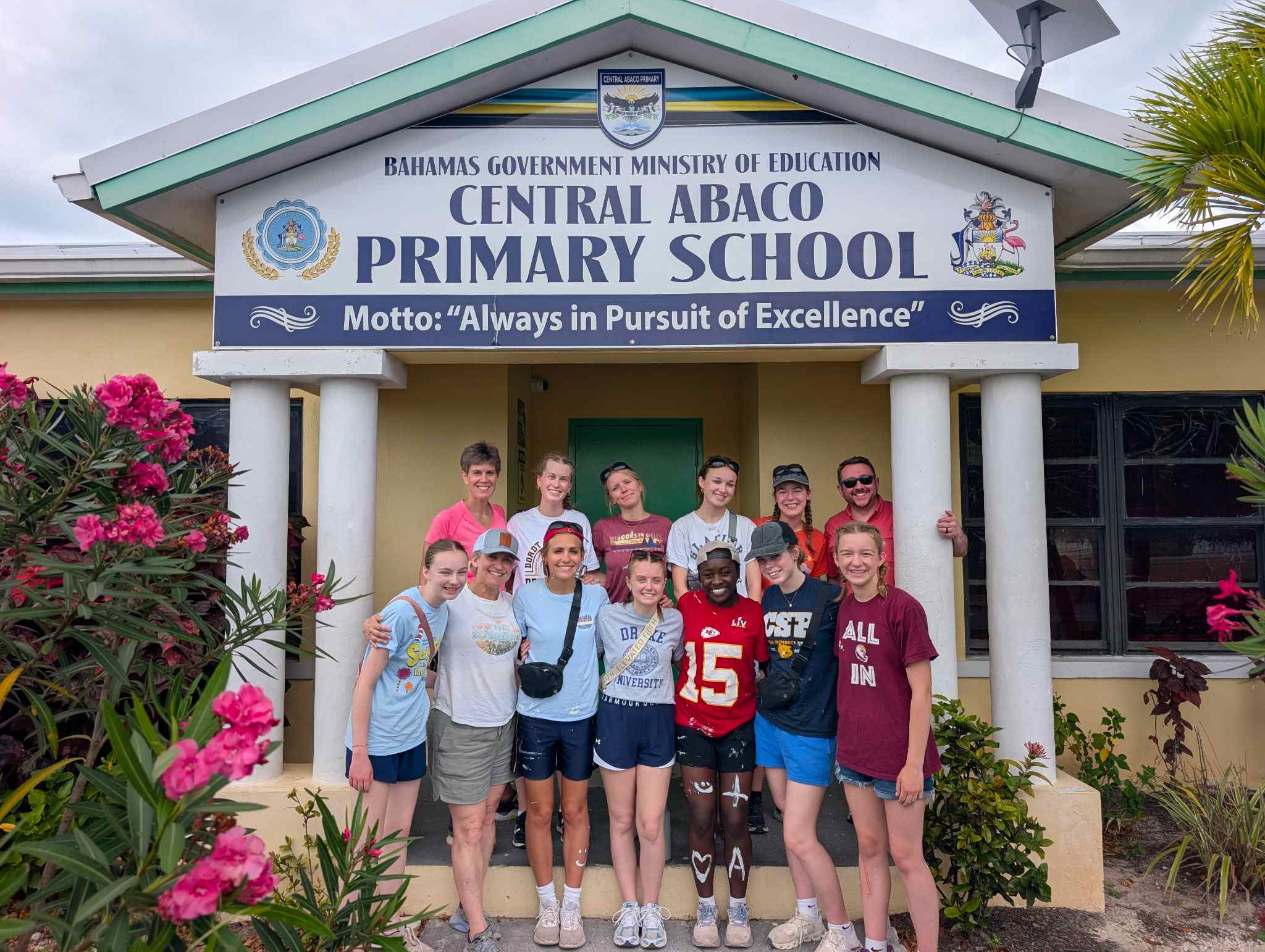 The Des Moines Christian School (DMC) impact team poses together under the entrance sign at Central Abaco Primary School (CAPS) during a youth mobilization and education trip with Many Hands.