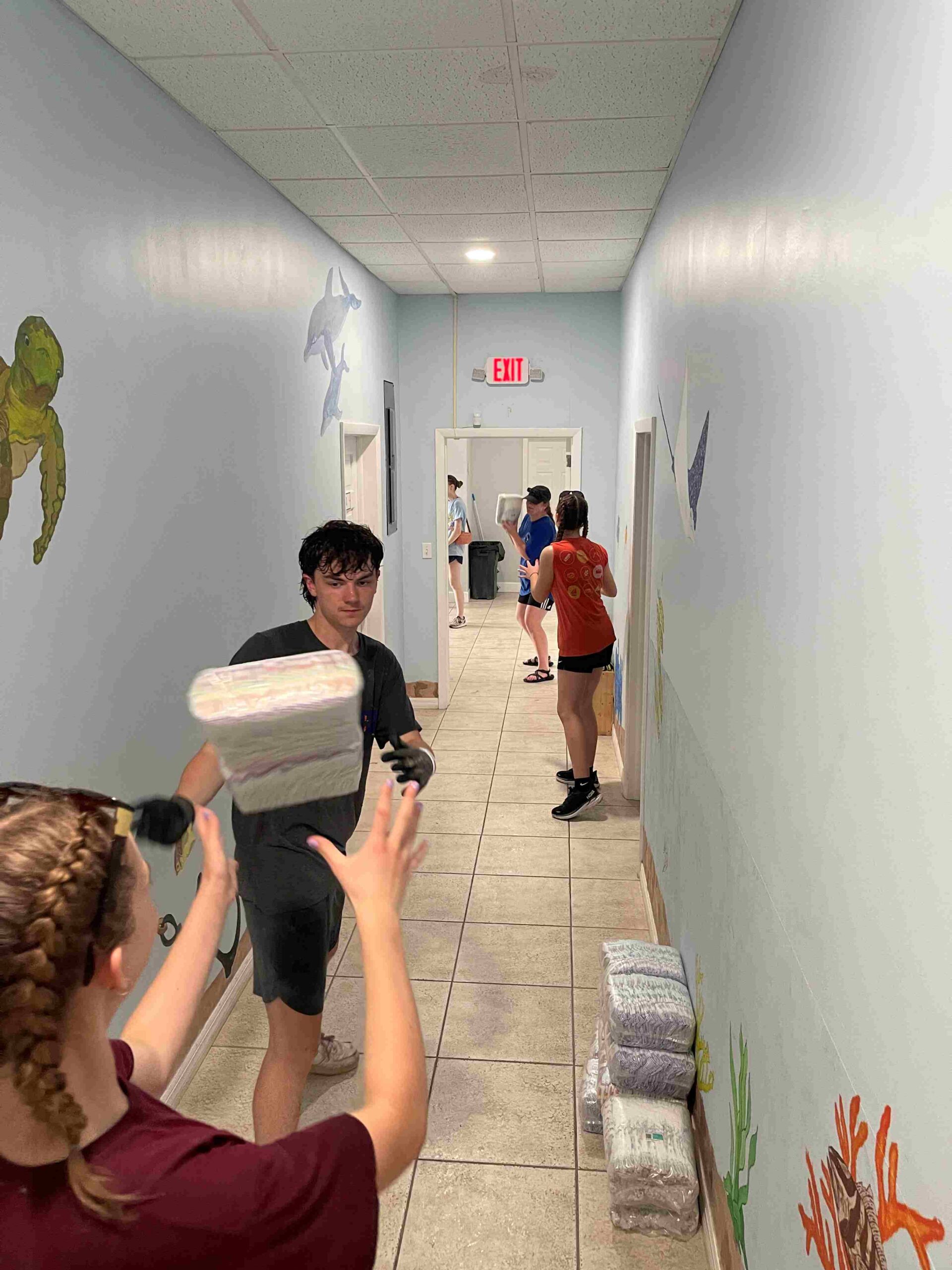 DMC student volunteers form a human assembly line down a school hallway to unload a shipment of donated diapers, partnering with a local church's compassion ministry in Abaco.