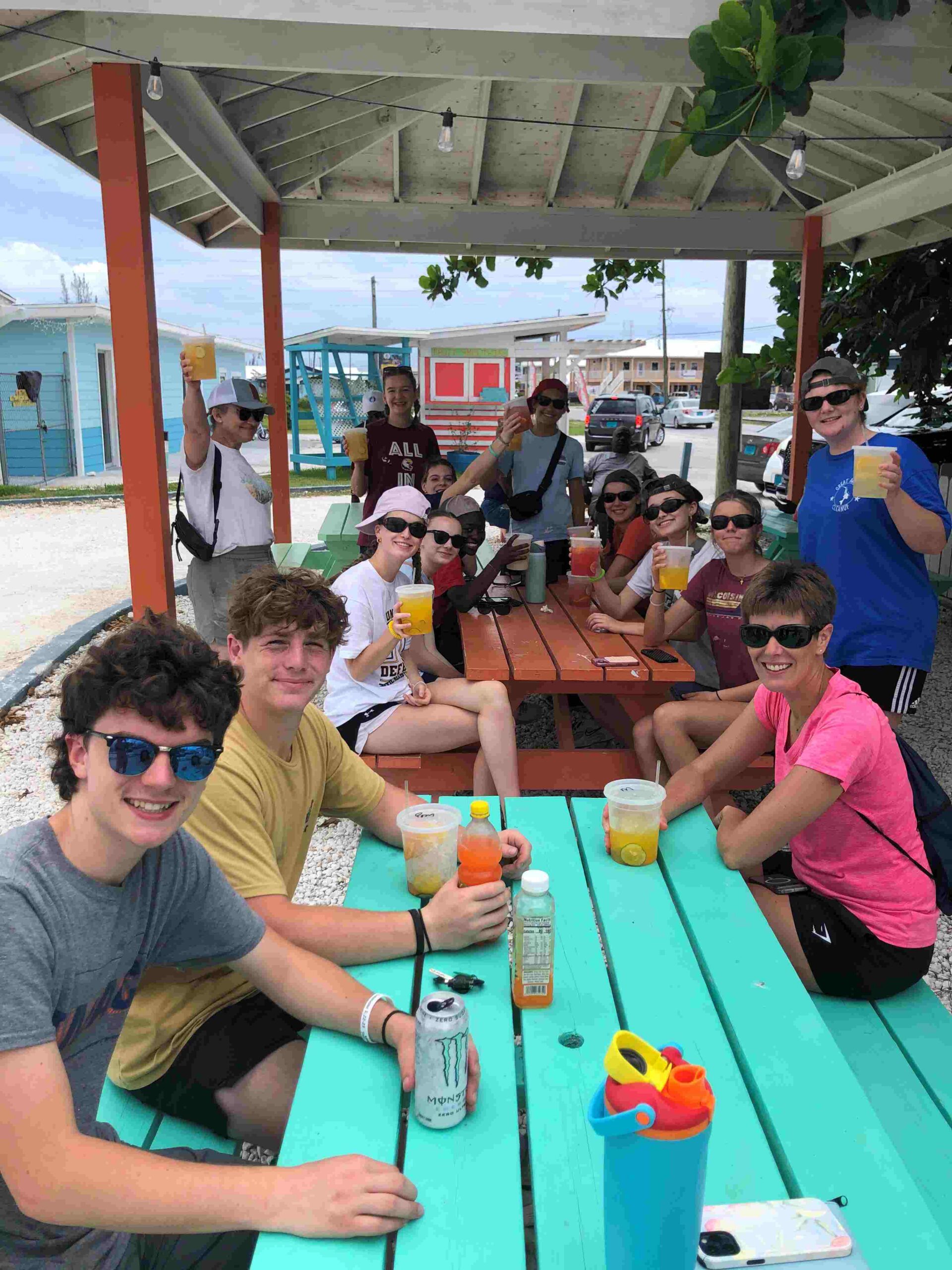 Many Hands volunteers from Des Moines Christian School take a quick break to support a local business, raising their glasses together at 'The Drink Machine' pavilion in Abaco.