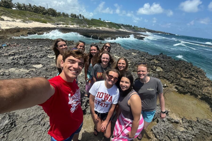 The Many Hands Kairos impact team smiles for a group photo on a rocky shore in Abaco, processing the visual and economic contrasts of the island during their Culture Day.