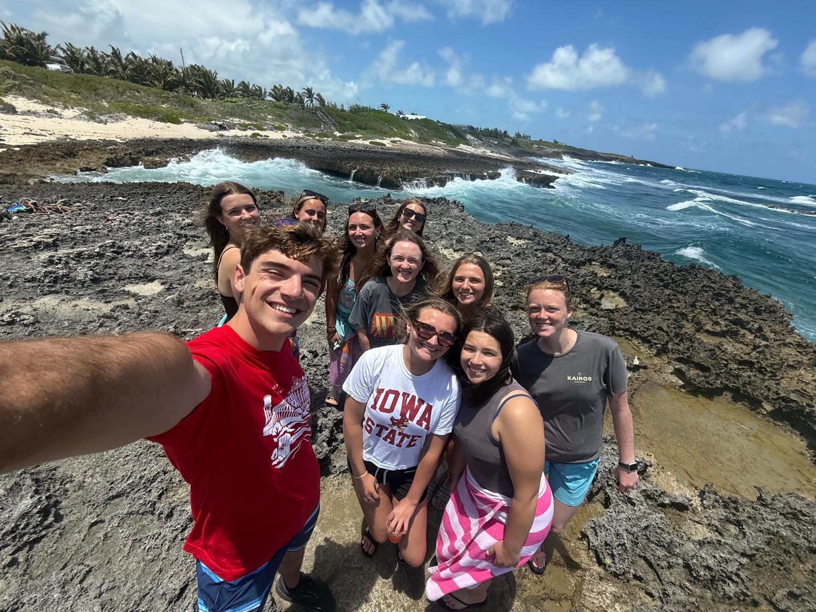 The Many Hands Kairos impact team smiles for a group photo on a rocky shore in Abaco, processing the visual and economic contrasts of the island during their Culture Day.