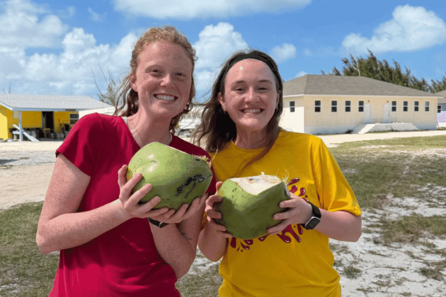 Two female volunteers from Lutheran Church of Hope Ames smile while holding fresh green coconuts, experiencing local hospitality and Bahamian culture on a Many Hands trip.