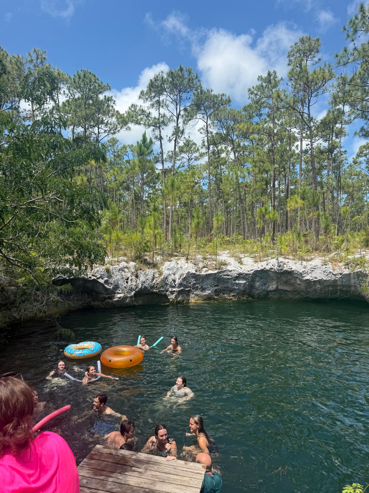 Kairos team members float and swim together in a deep freshwater blue hole, experiencing the natural beauty of Abaco as part of a Many Hands cultural immersion day.