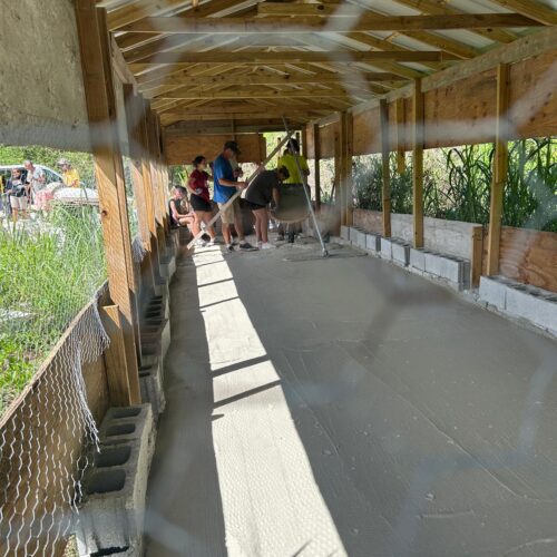 Many Hands Kairos team members smooth freshly poured concrete inside a new chicken coop building, helping rebuild vital agricultural infrastructure on an Abaco farm.
