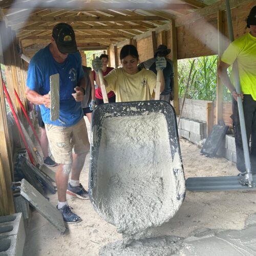 Kairos team members work together to tilt a wheelbarrow filled with wet cement, constructing a concrete floor for a hurricane-devastated farm in Abaco.