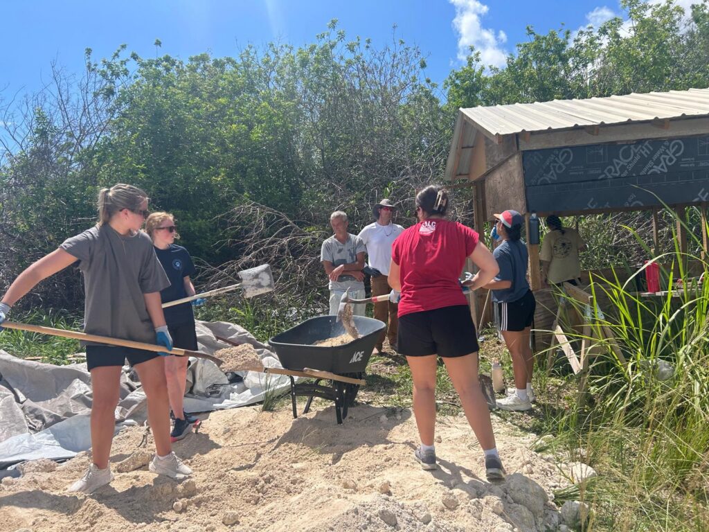 Many Hands team members shovel sand and gravel to mix concrete, dedicating their labor to help local entrepreneurs rebuild their livelihoods after the hurricanes.