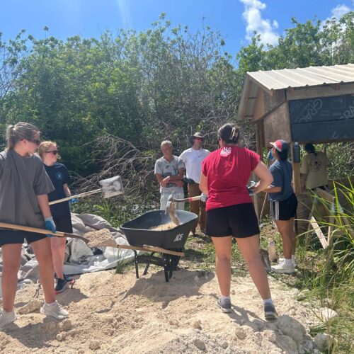 Many Hands team members shovel sand and gravel to mix concrete, dedicating their labor to help local entrepreneurs rebuild their livelihoods after the hurricanes.