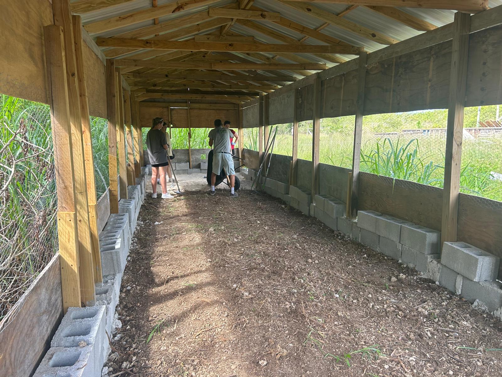 The Many Hands Kairos impact team from Lutheran Church of Hope Ames works inside a chicken house to level dirt and prep the floor for a new chicken coop on a local farm in Abaco.