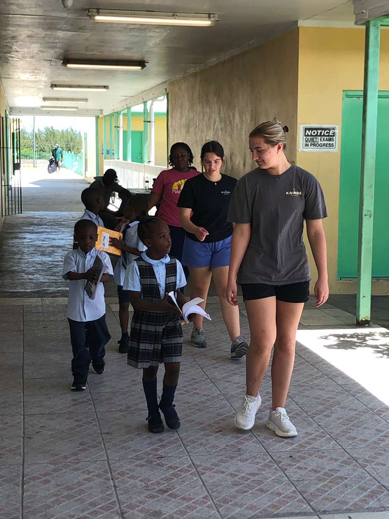 Volunteers from the Many Hands Kairos impact team accompany young students walking through the hallway of Central Abaco Primary School (CAPS) during an Impact Trip.