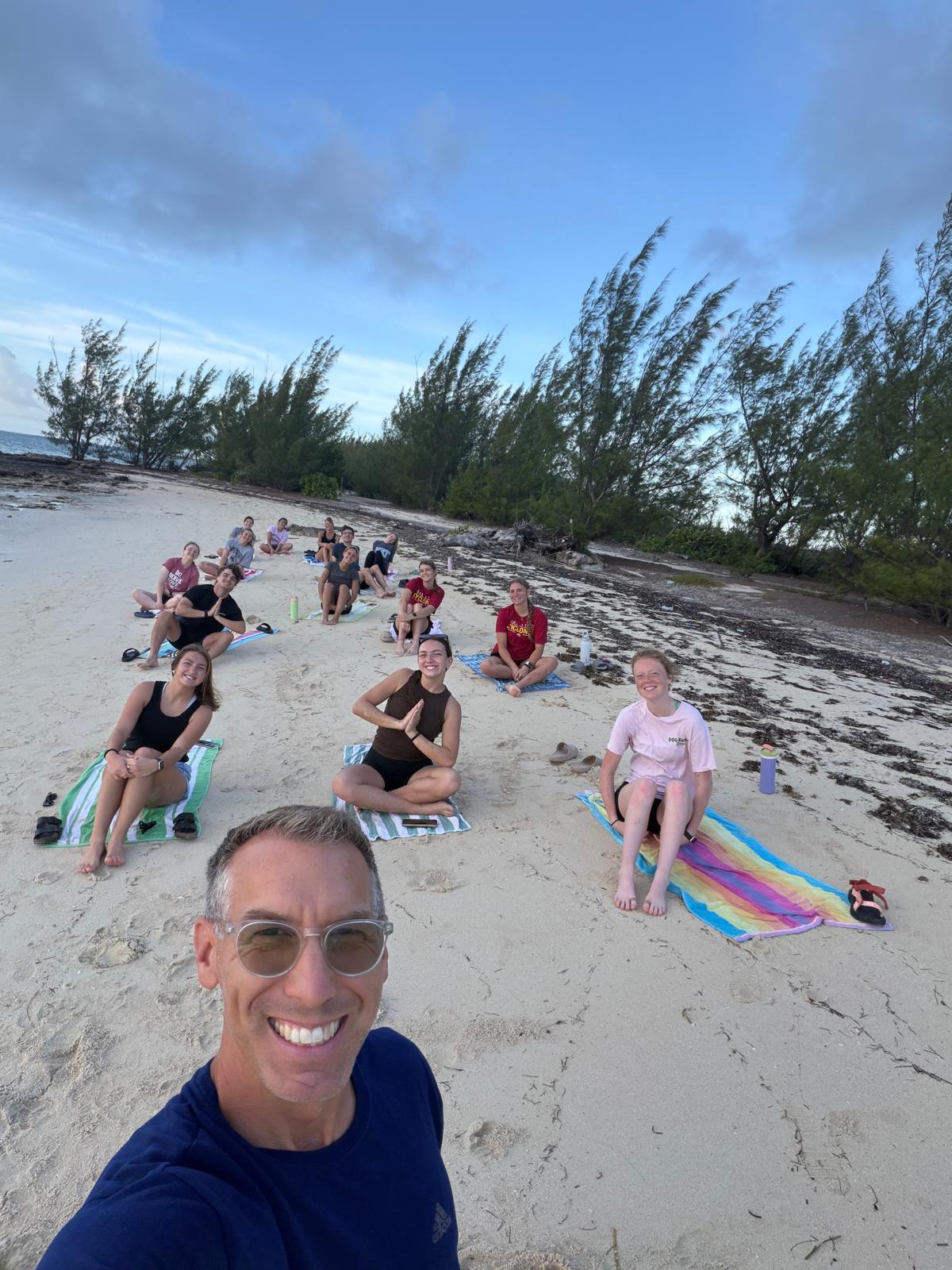 The Many Hands Kairos team gathers on a beach in Abaco for a morning devotion and stretching session, moving away from cultural distractions to focus on experiential faith.