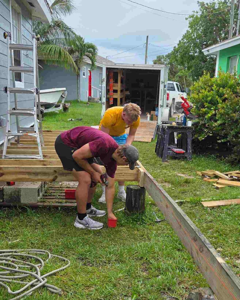 Volunteers from the Immanuel CRC Youth Impact Team work together outdoors to build a new wooden deck frame, advancing a Safe Structures home rebuilding project in Abaco.