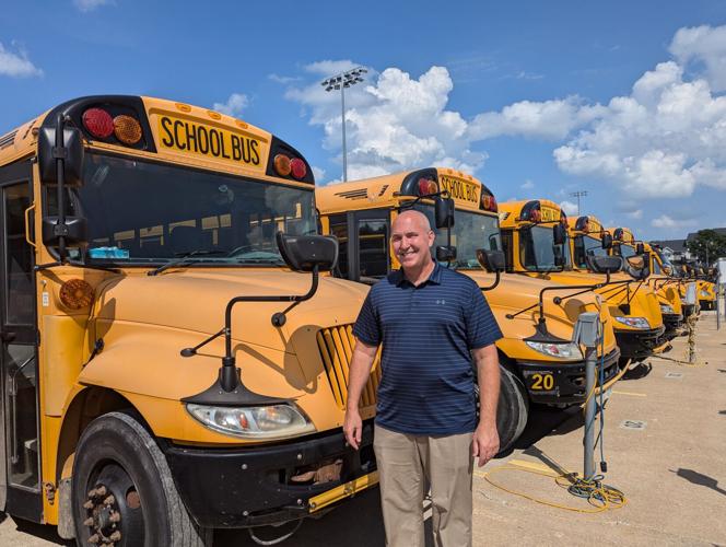 Greg Ebeling stands next to a row of yellow school buses, drawing on his 13-year tenure as Superintendent of Pella Community Schools to champion global education and infrastructure.