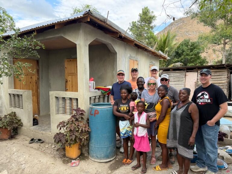 An vision team stands with a local Haitian family outside their newly constructed cement house, representing the Many Hands Safe Structures program and the transformational power of strategic donor investments.