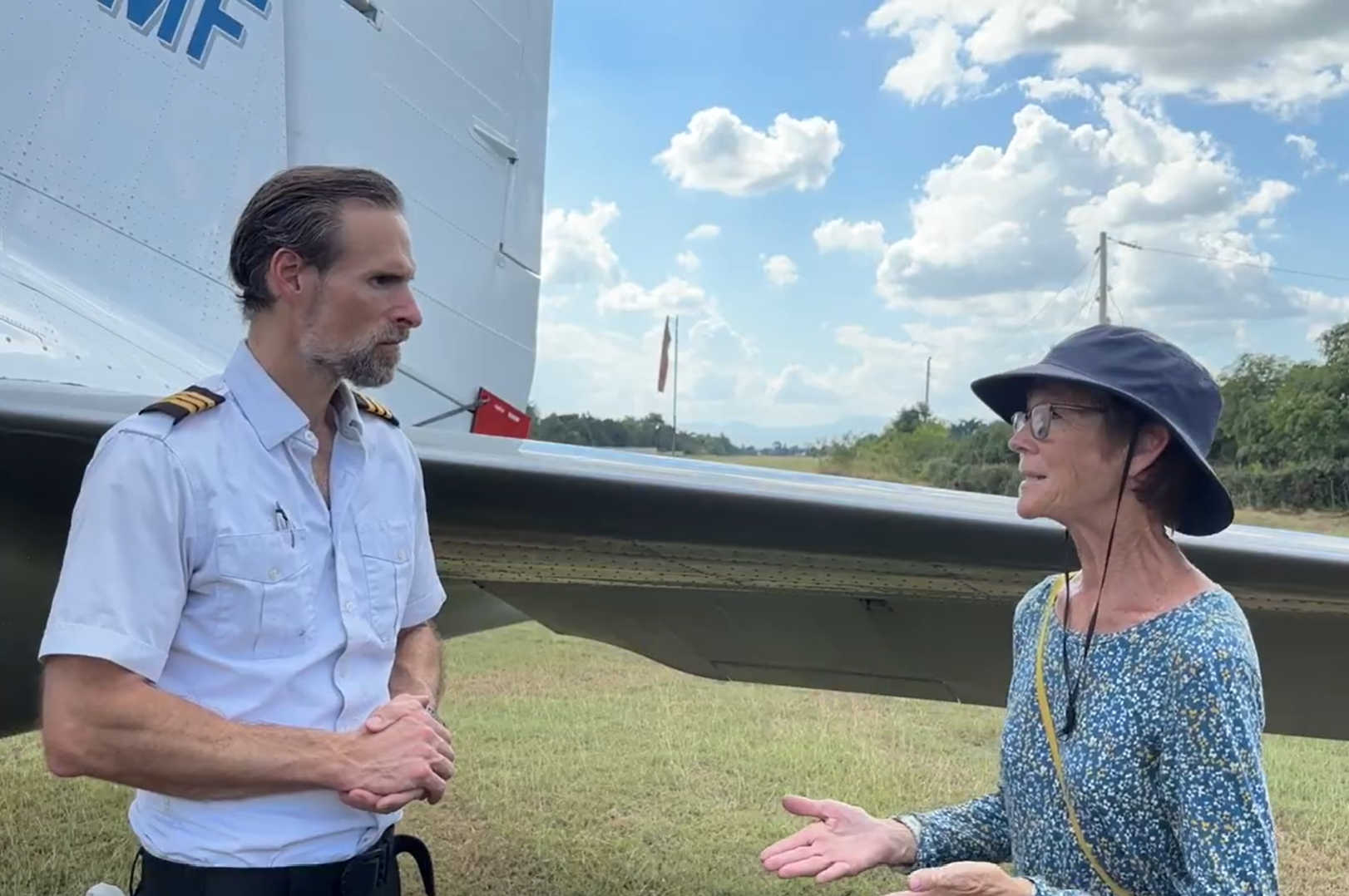 Many Hands missionary Christi Gabhart participates in a grass runway interview next to a missionary airplane, discussing local empowerment and sustainable international development models in Haiti.