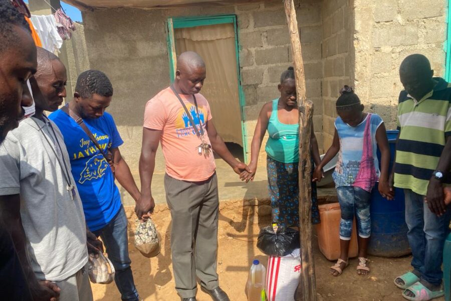 Haitian staff members from the Many Hands team hold hands in a prayer circle with a local family during a neighborhood home visit and food supply delivery in Pignon, Haiti.