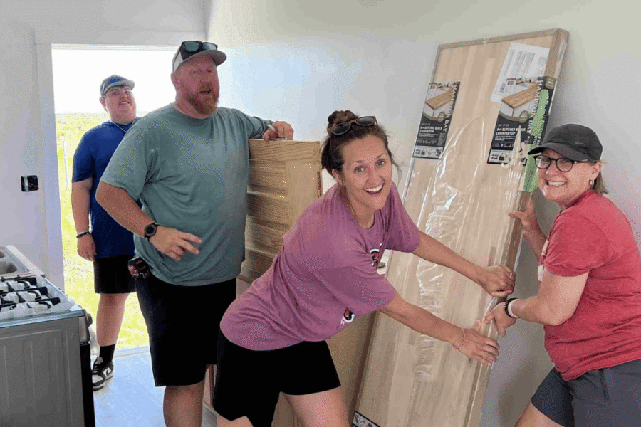 Celebrate Church Impact team members smile as they hold new flooring that they are installing to complete a Many Hands Safe Homes project.
