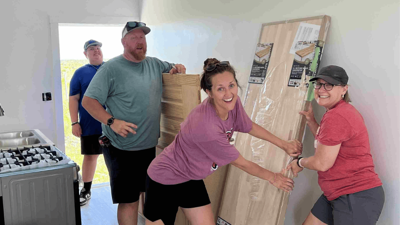 Celebrate Church Impact team members smile as they hold new flooring that they are installing to complete a Many Hands Safe Homes project.