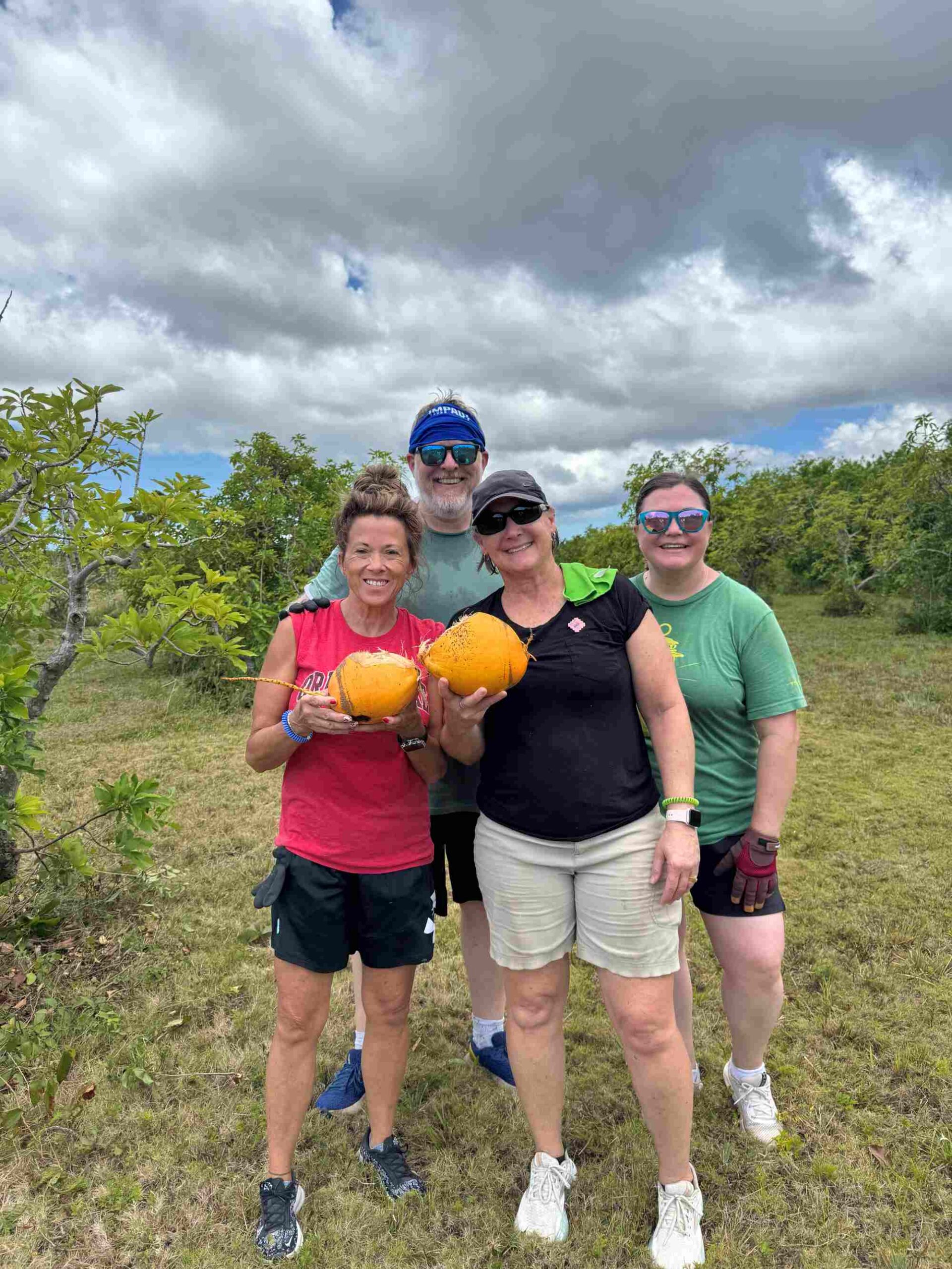 Short-term mission trip volunteers pose with fresh coconuts during a farm cleanup project, highlighting cultural immersion and team fellowship with Many Hands.
