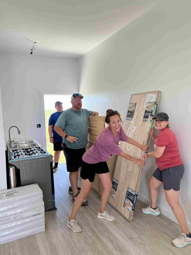Celebrate Church Impact team members smile as they hold new flooring that they are installing to complete a Many Hands Safe Homes project.