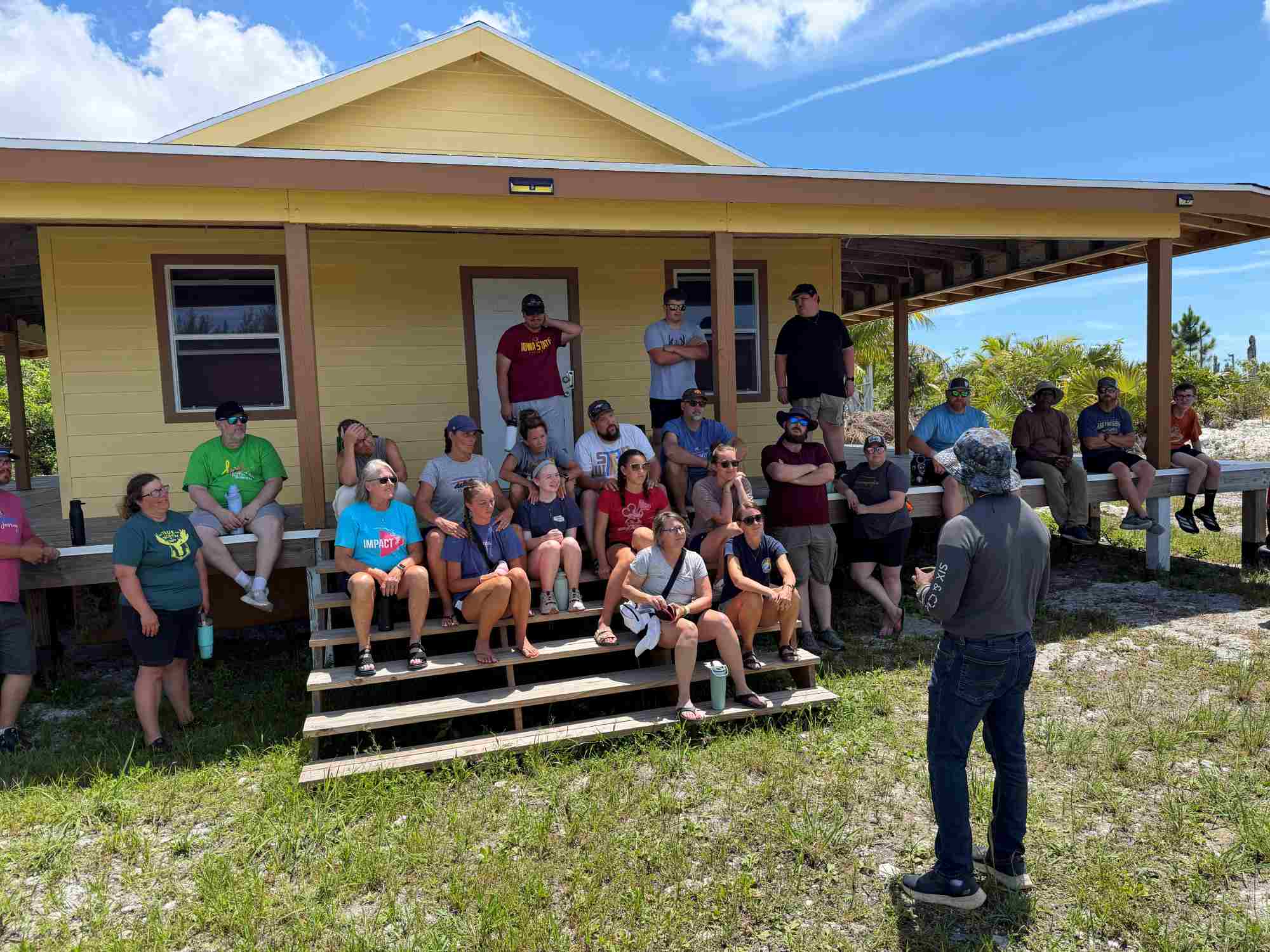 Celebrate Church short-term volunteers gather on the porch steps to listen to a local pastor's story of hope and structural rebuilding after Hurricane Dorian.