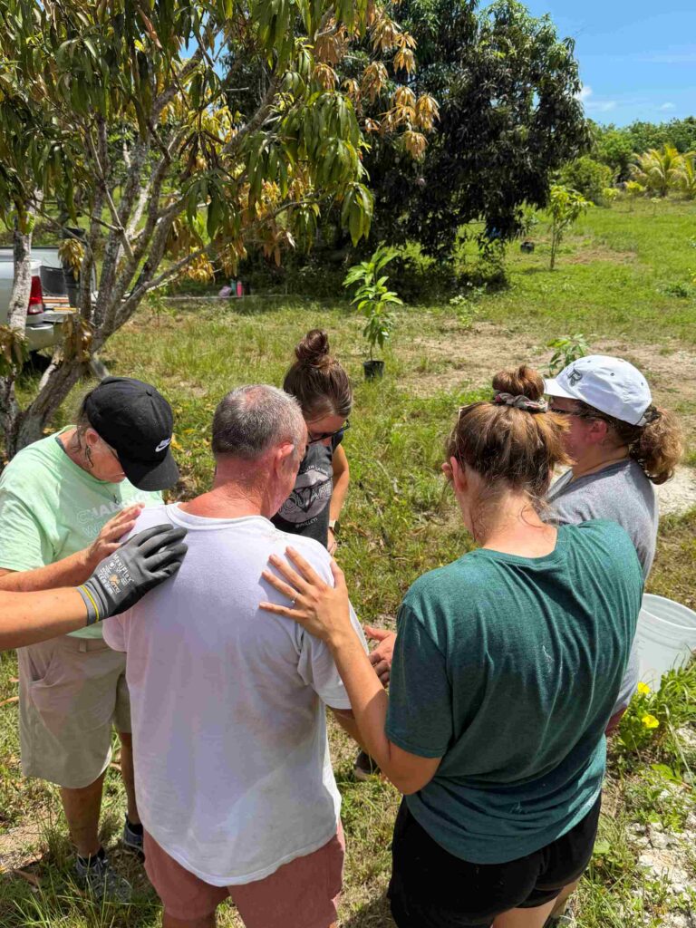 Impact team participants bow their heads and lay hands on a local resident to pray during a farm restoration and agricultural partnership visit.