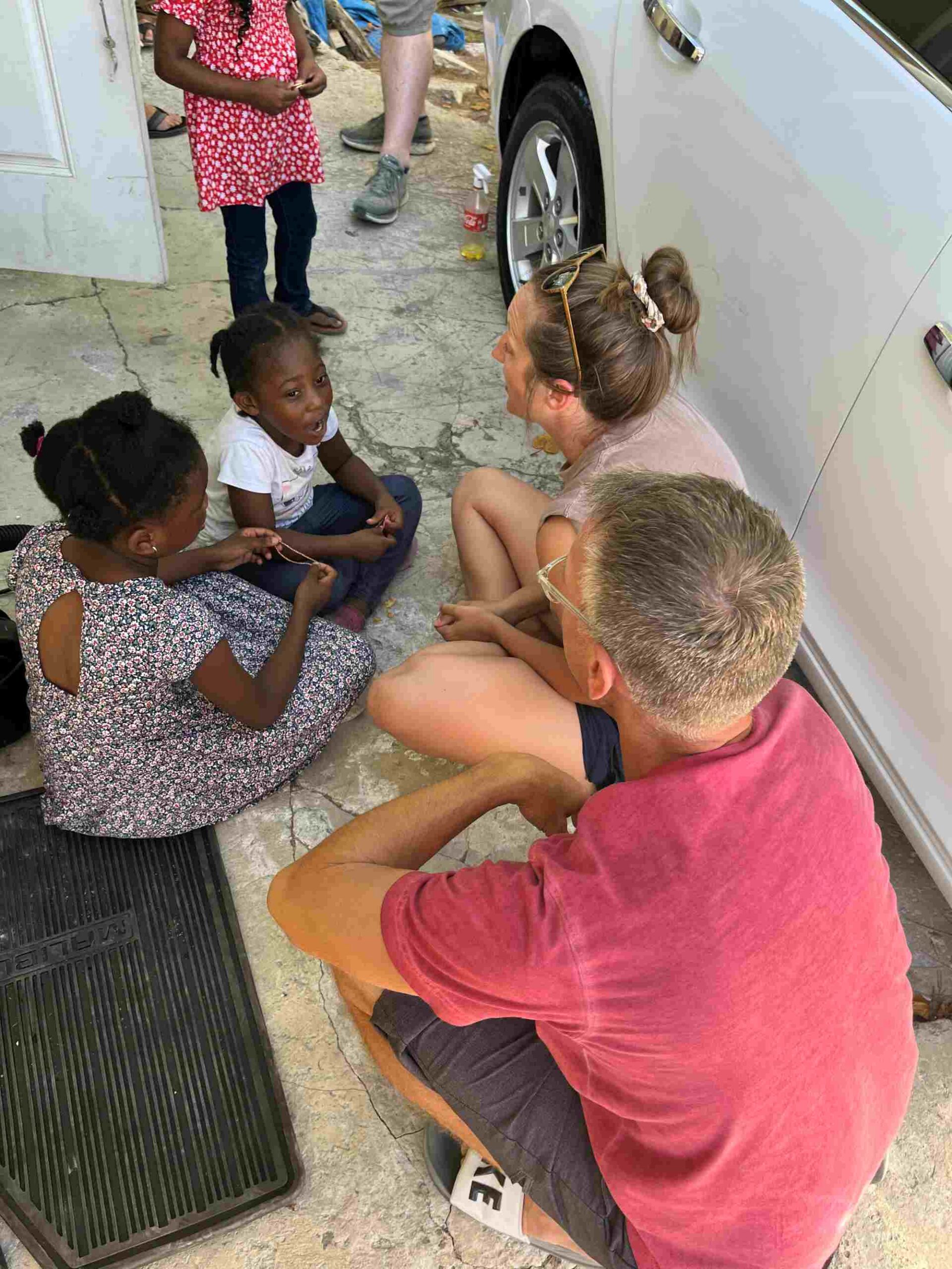 Many Hands volunteers sit on the ground to talk and connect intentionally with local children during a neighborhood food distribution ministry in Abaco.