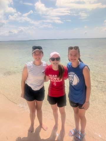 Three Des Moines Christian School student volunteers smile together on the shore of Camp Abaco, reflecting on a week of heart transformation, service, and community connection.