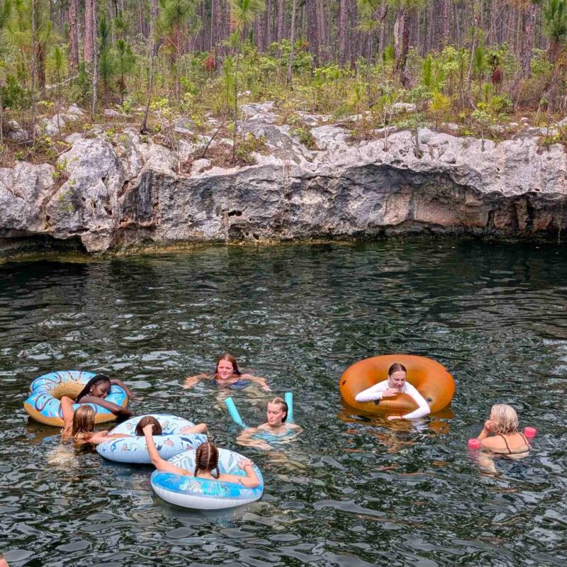 Volunteers from the Des Moines Christian School impact team float on inner tubes and swim together in an Abaco blue hole during a cultural immersion day with Many Hands.