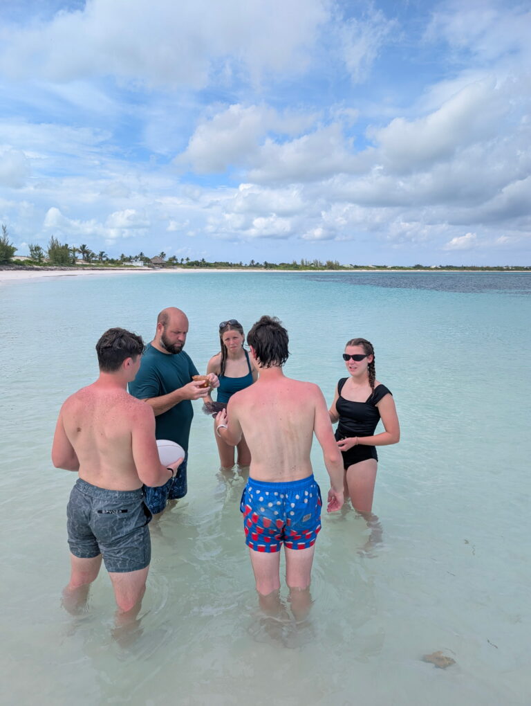 DMC youth team members stand in shallow turquoise water to learn about native marine life and sustainable island ecosystems during an Abaco culture day.
