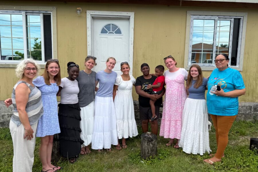 Des Moines Christian School student volunteers stand hand-in-hand with Spring City community members outside a local home, embodying Many Hands' mission of relational connection and life development.