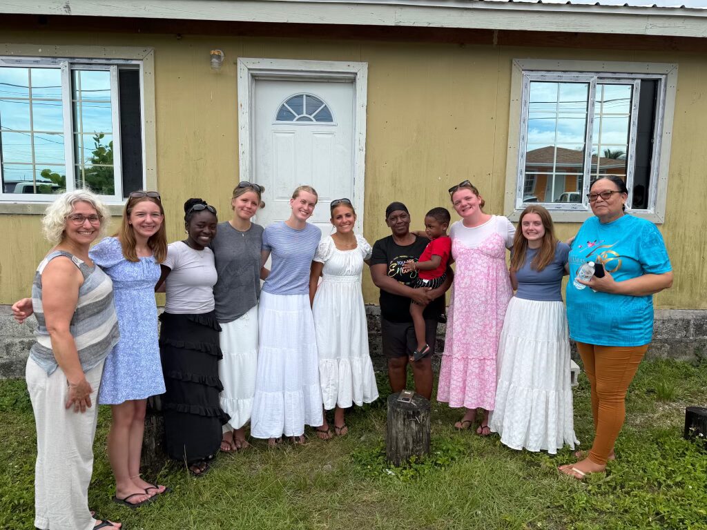 Des Moines Christian School student volunteers stand hand-in-hand with Spring City community members outside a local home, embodying Many Hands' mission of relational connection and life development.