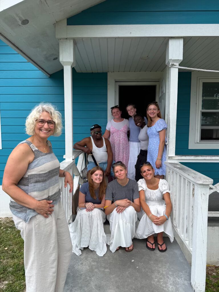 DMC impact team volunteers smile alongside a local resident on a bright blue porch in Spring City, Abaco, highlighting the mutual joy and reciprocal blessings of Many Hands food distribution visits.
