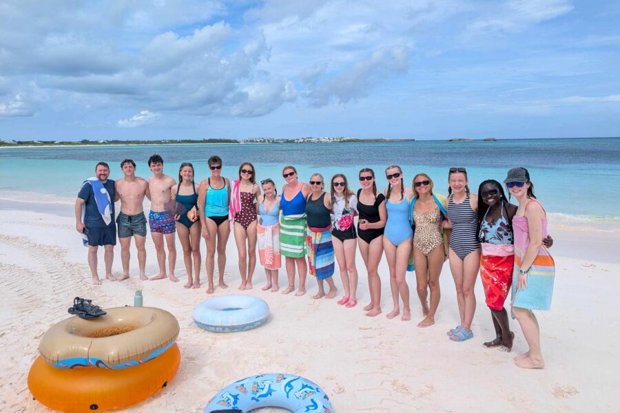 The DMC student impact team stands together on the white sands of Winding Bay, experiencing the natural beauty of the Bahamas on a Many Hands team-building trip.