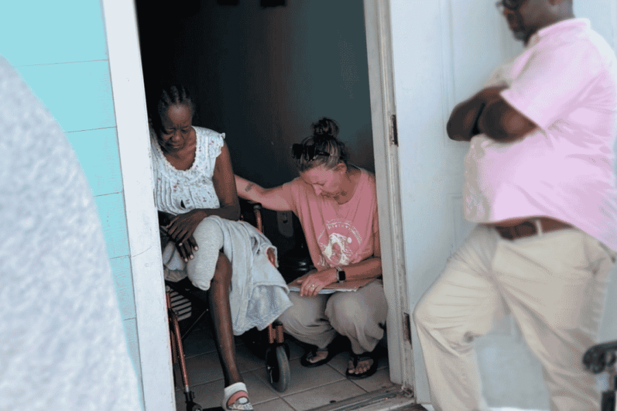 A Many Hands trip leader places a hand on a local resident's shoulder to pray during a Sunday food distribution home visit in Abaco, Bahamas.