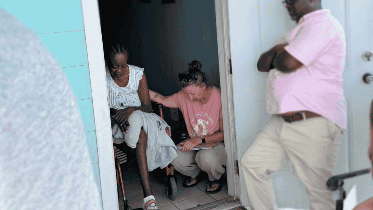 A Many Hands trip leader places a hand on a local resident's shoulder to pray during a Sunday food distribution home visit in Abaco, Bahamas.