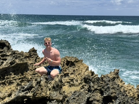 An impact trip participant pauses on a rugged rock formation along the Abaco coastline during a team rest and cultural immersion day.