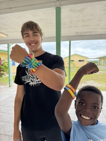 A student volunteer and a young Bahamian boy smile proudly while showing off their matching colorful wristbands during a school mentorship day.