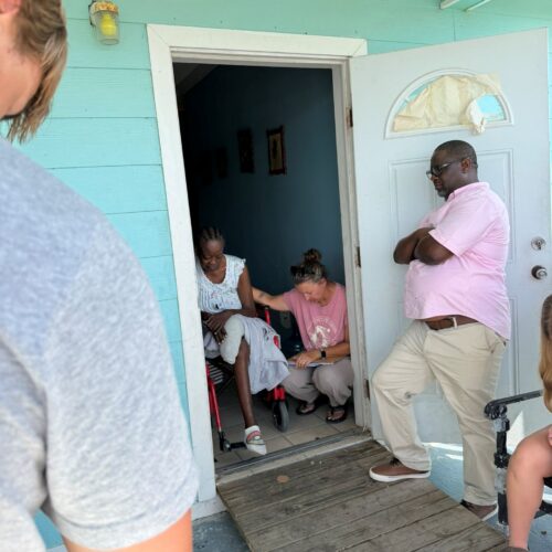 A Many Hands trip leader places a hand on a local resident's shoulder to pray during a Sunday food distribution home visit in Abaco, Bahamas.