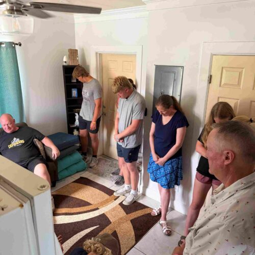 Immanuel CRC youth group members bow their heads in a tight circle to pray over a local family inside their home during a community outreach day with Many Hands.