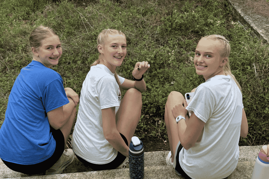 Three female youth team members from Sheldon, Iowa, smile together during a break from service, processing their experiences of cross-cultural fellowship on an Abaco impact trip.