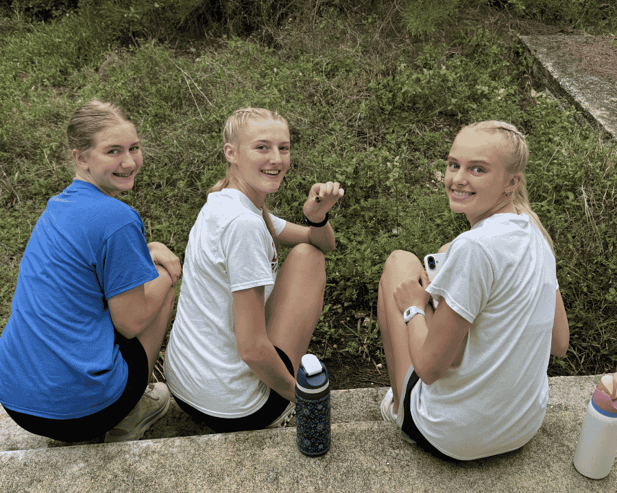 Three female youth team members from Sheldon, Iowa, smile together during a break from service, processing their experiences of cross-cultural fellowship on an Abaco impact trip.