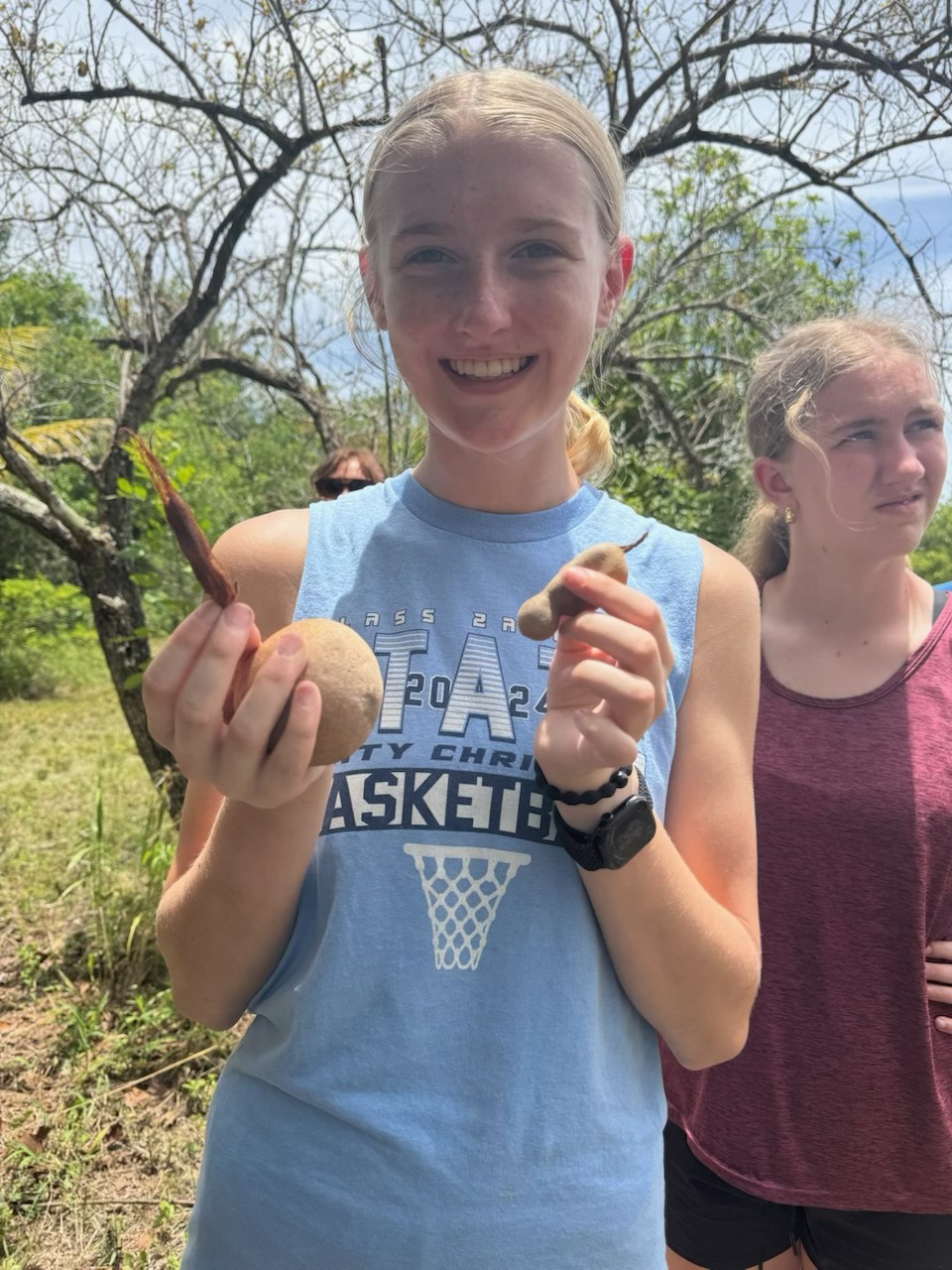 A youth volunteer smiles while displaying freshly harvested local produce, exploring native Bahamian agriculture during an intentional cultural learning day.